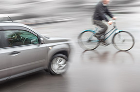 blurred image of a car going toward a bicyclist for the bike accident page for Heintz & Becker